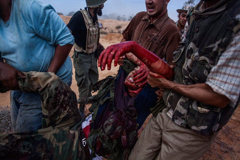 Libyan rebels carry a severely wooded comrade after being hit by friendly fire of a a tank  during clashes against the Libyan Army near the city of Sirte, Libya, October 2011.